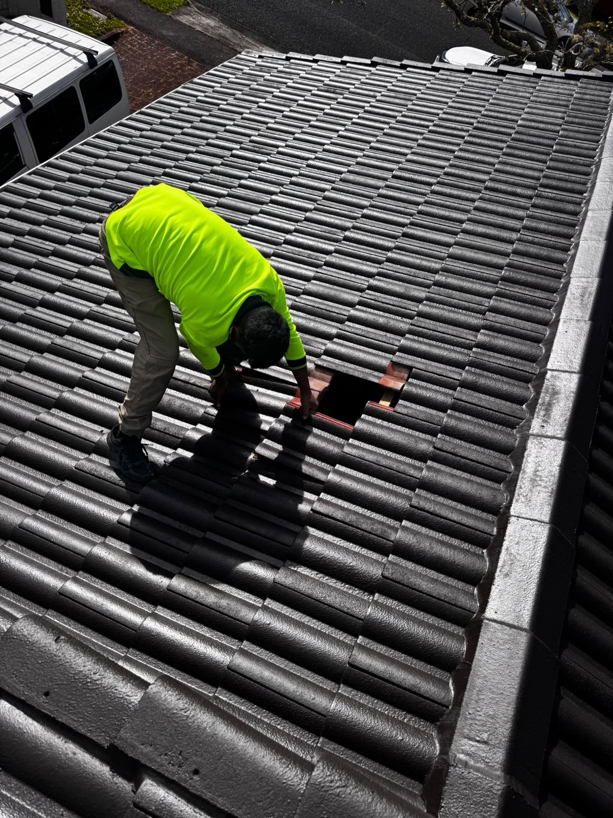 Crew member replacing broken concrete tiles on a house roof